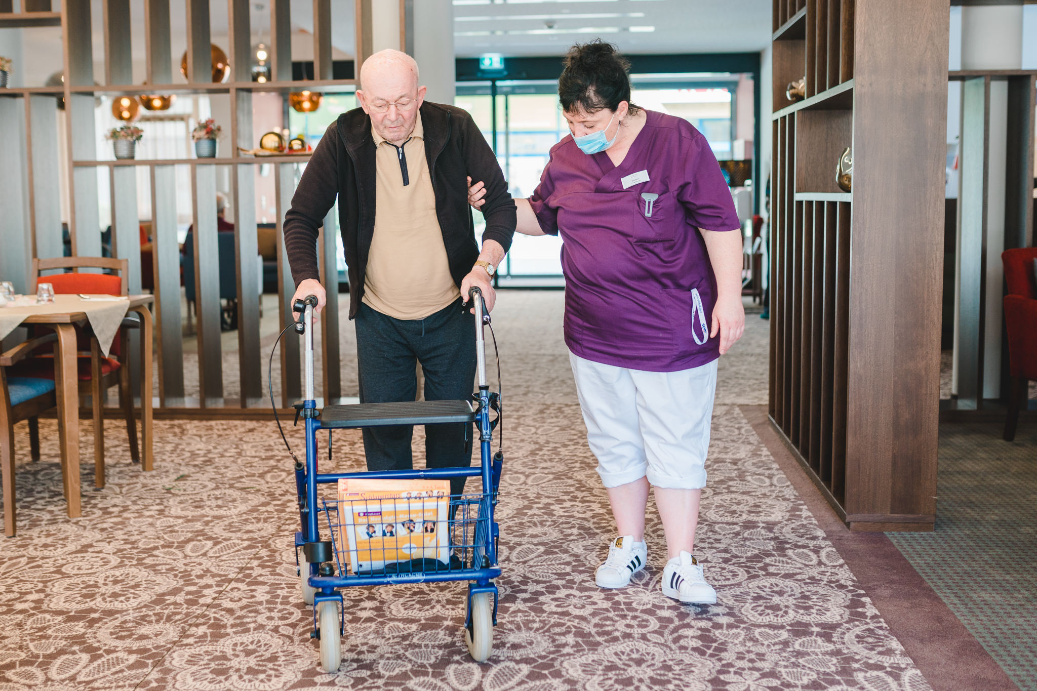 Pflegepersonal unterstützt älteren Bewohner mit Rollator