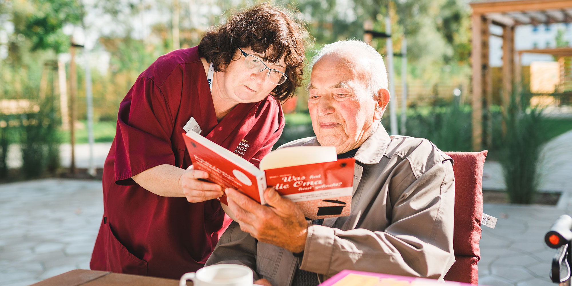 Eine Betreuungsassistenz schaut mit einem Bewohner ein Buch an.